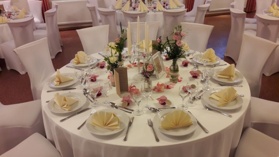 runder Tisch mit weißer Tischdecke, Servietten und Blumenschmuck in Pastellgelb und -rosa