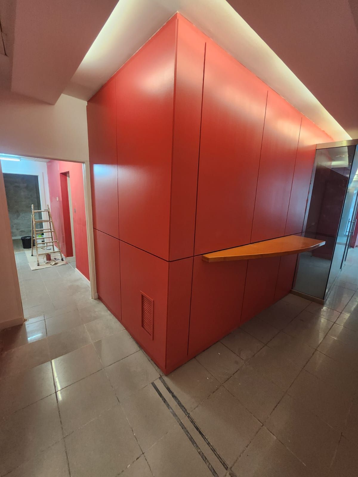 Un pasillo con una pared roja y un estante de madera.