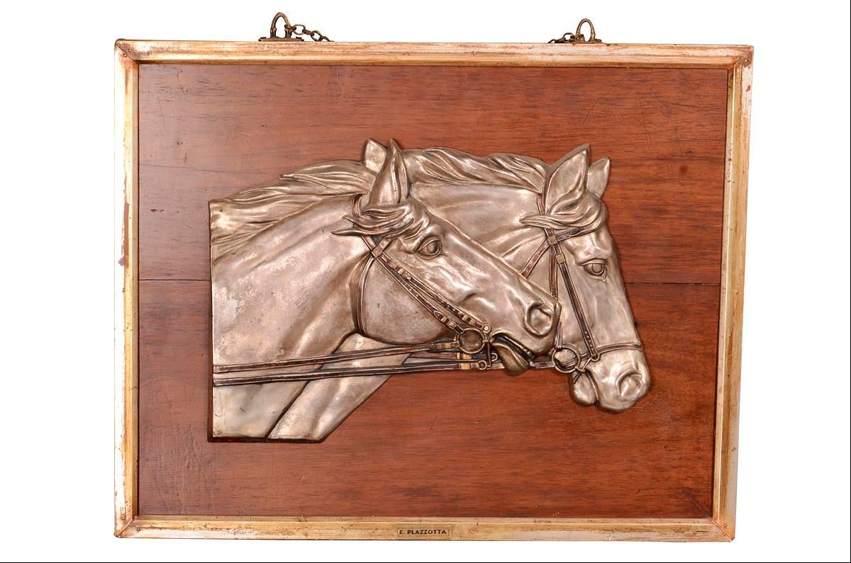 Silbernes Relief mit Pferdekopf-Motiv auf einer dunklen Holzplatte.