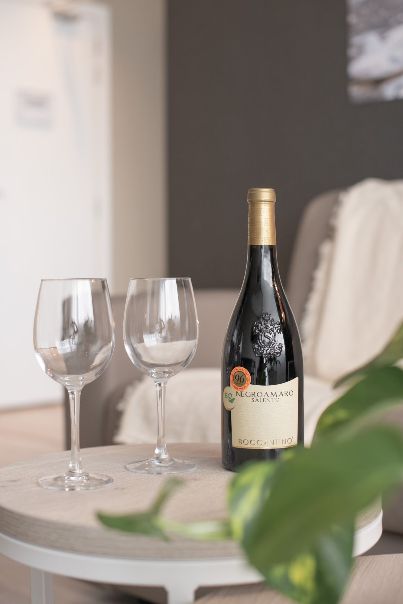 Een fles rode wijn en twee lege wijnglazen staan op tafel, voor de bank.