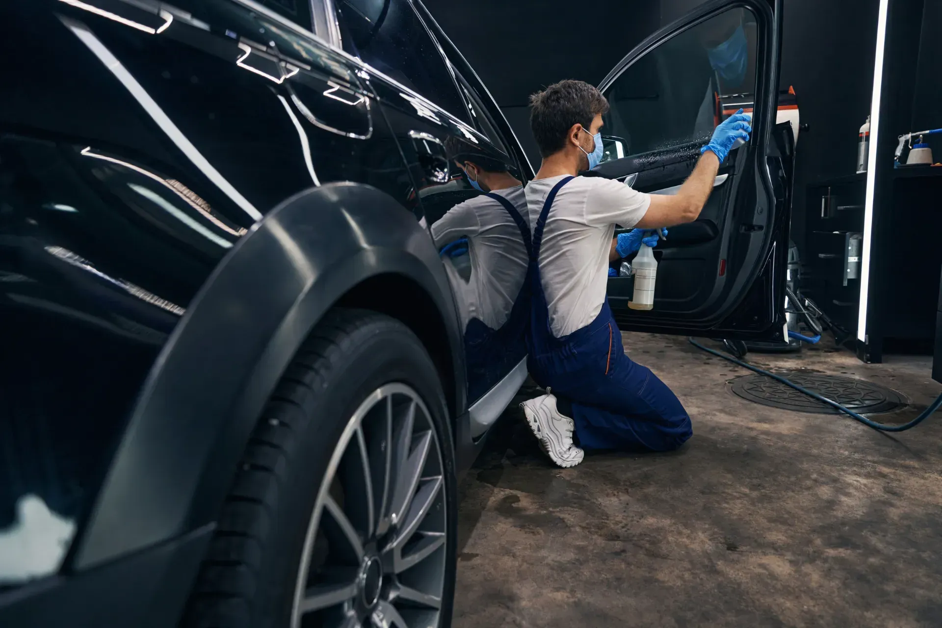 Un hombre está arrodillado frente a un coche negro.