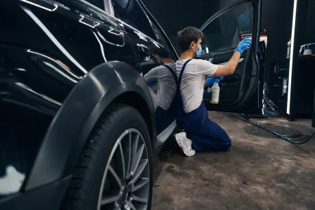 Un hombre está arrodillado frente a un coche negro.