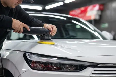 Un hombre está puliendo un coche blanco con una máquina.