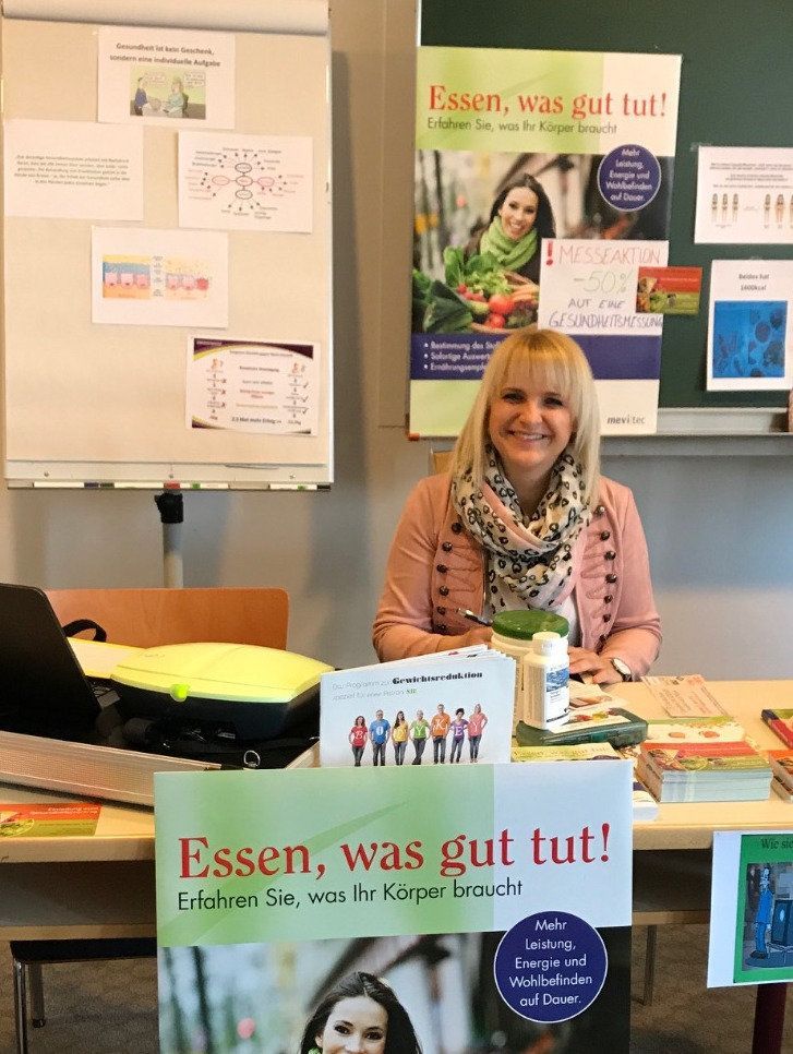 Eine Frau sitzt an einem Tisch mit einem Schild mit der Aufschrift „Essen was gut tut!“