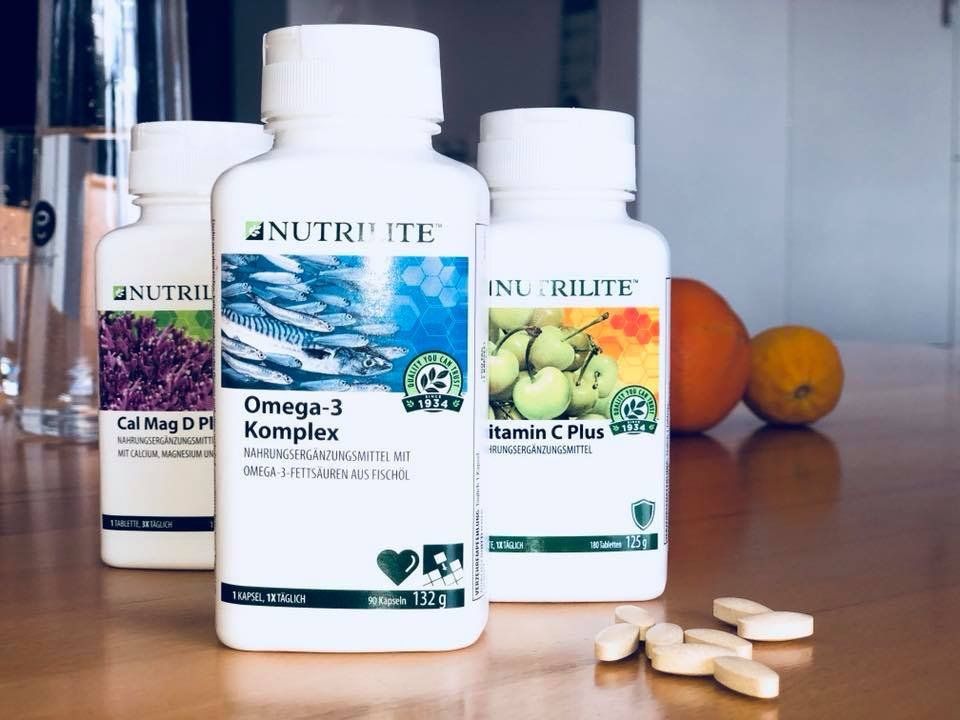 Auf einem Holztisch stehen drei Flaschen Nutrilite-Vitamine.