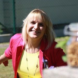 Eine Frau in einem gelben Hemd und einer roten Jacke lächelt.