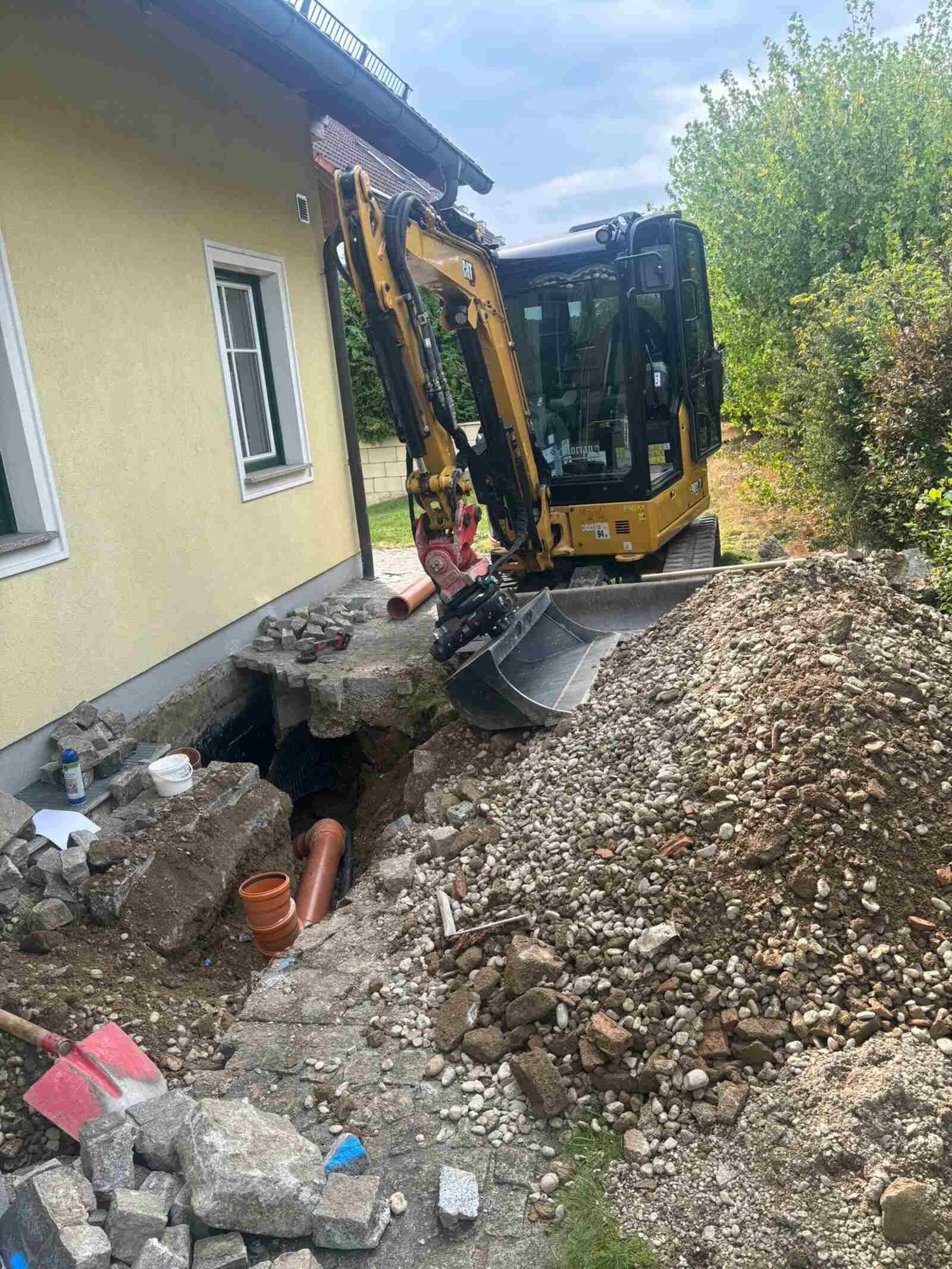 Ein gelber Bagger gräbt vor einem Haus ein Loch.