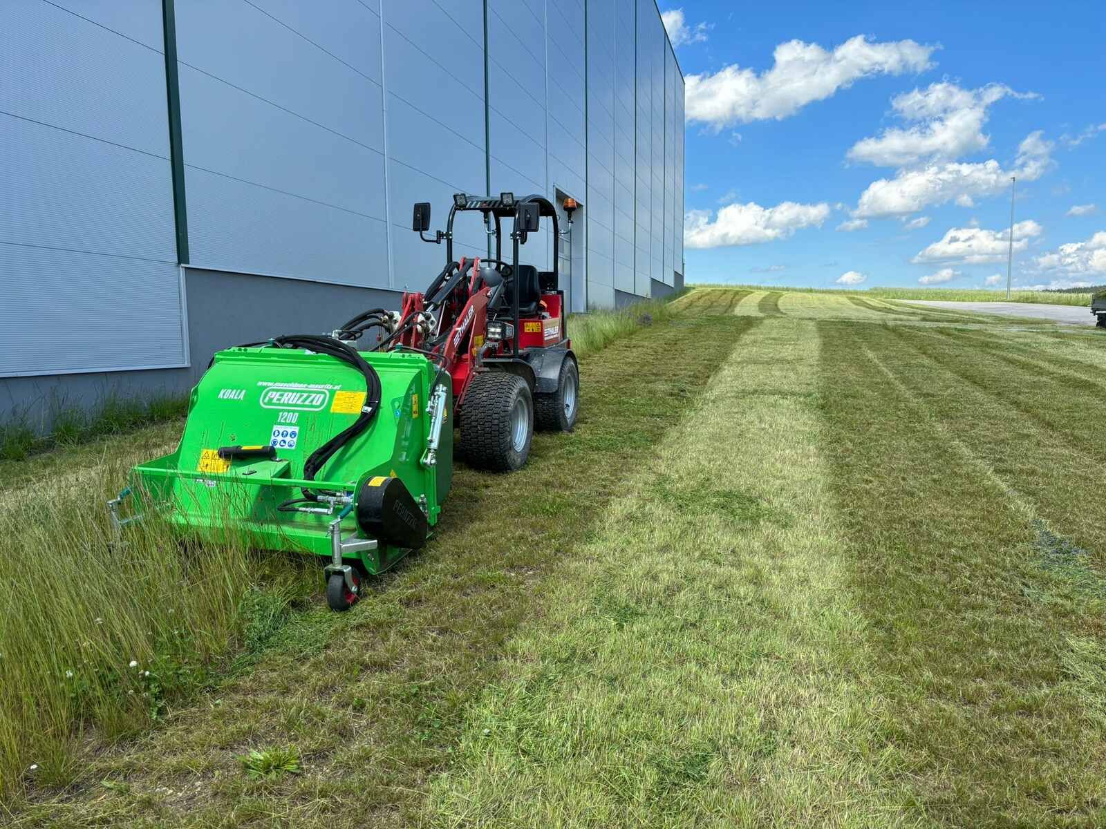Ein grüner Traktor mäht Gras vor einem Gebäude.