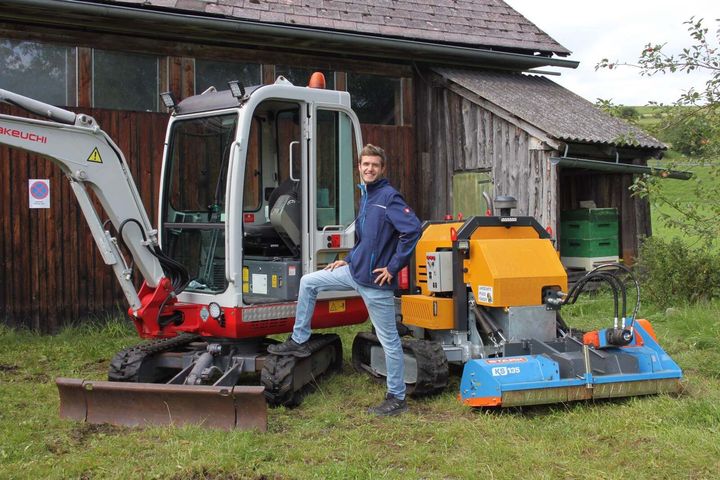Ein Mann sitzt auf einem kleinen Bagger neben einer kleinen Maschine.