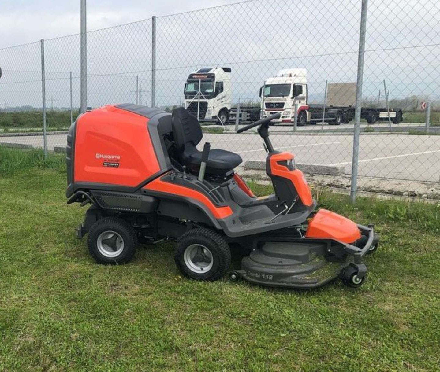 Ein Rasenmäher ist auf einer Wiese neben einem Maschendrahtzaun geparkt.