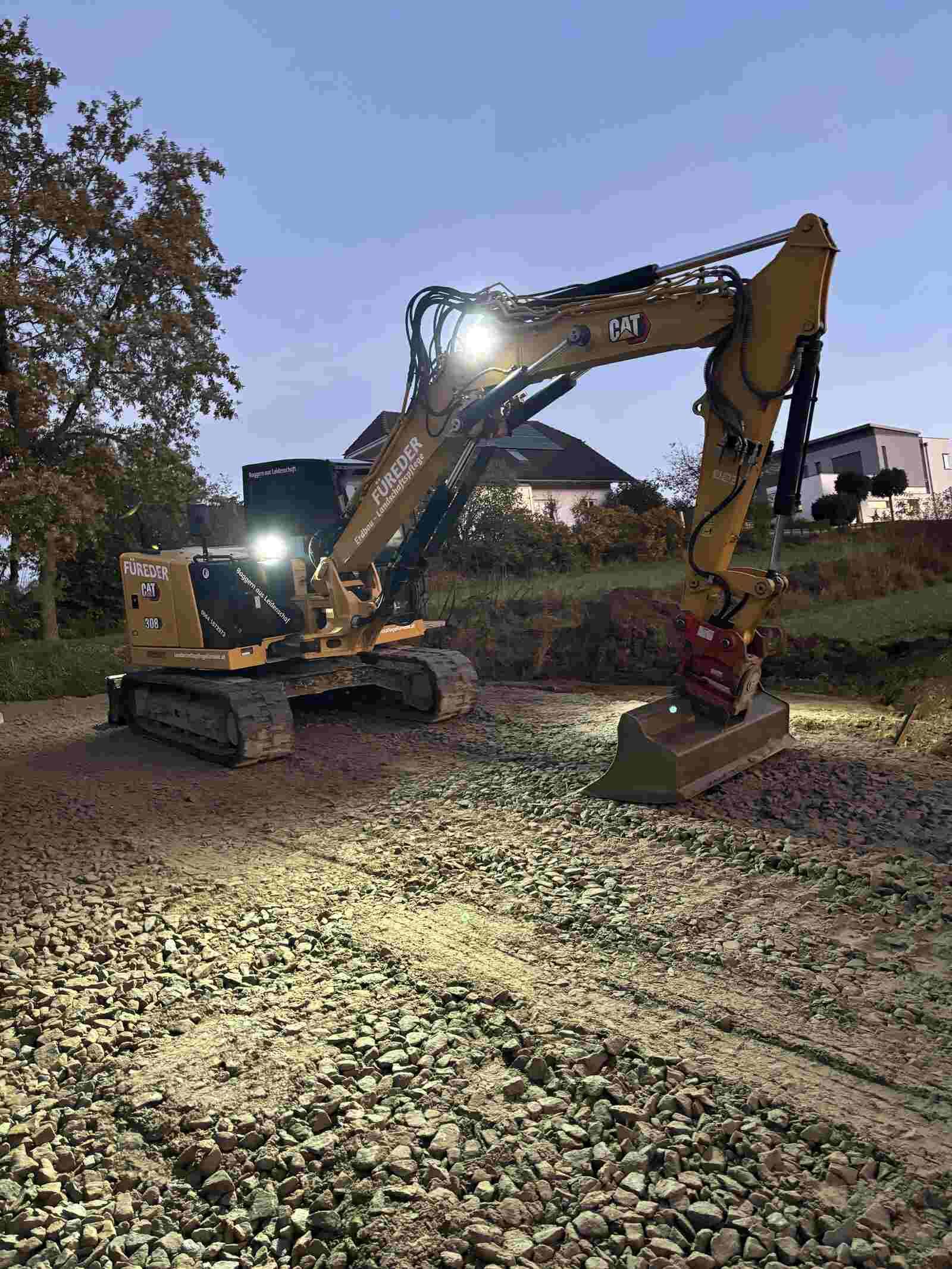 Ein gelber Bagger steht nachts auf einer Schotterstraße.