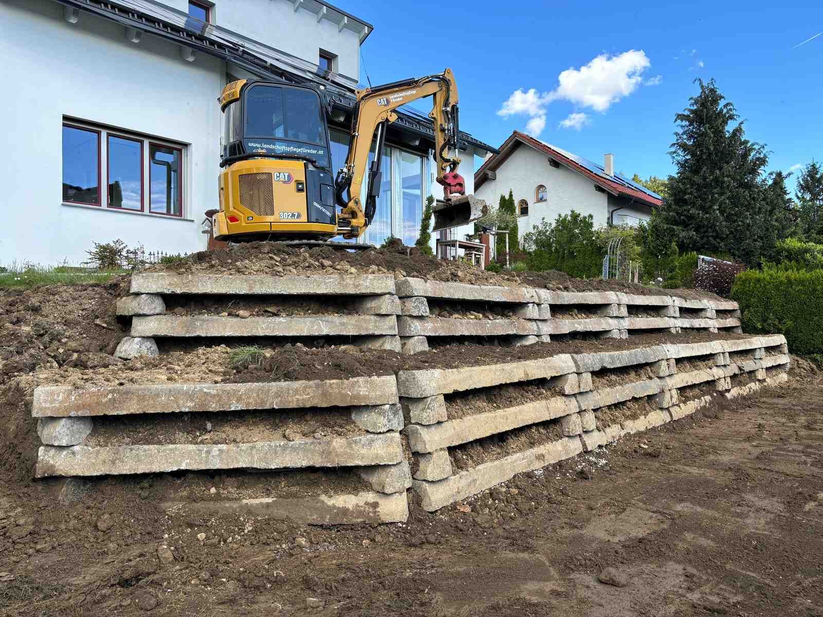 Ein gelber Bagger steht auf einem Erdhaufen vor einem Haus.