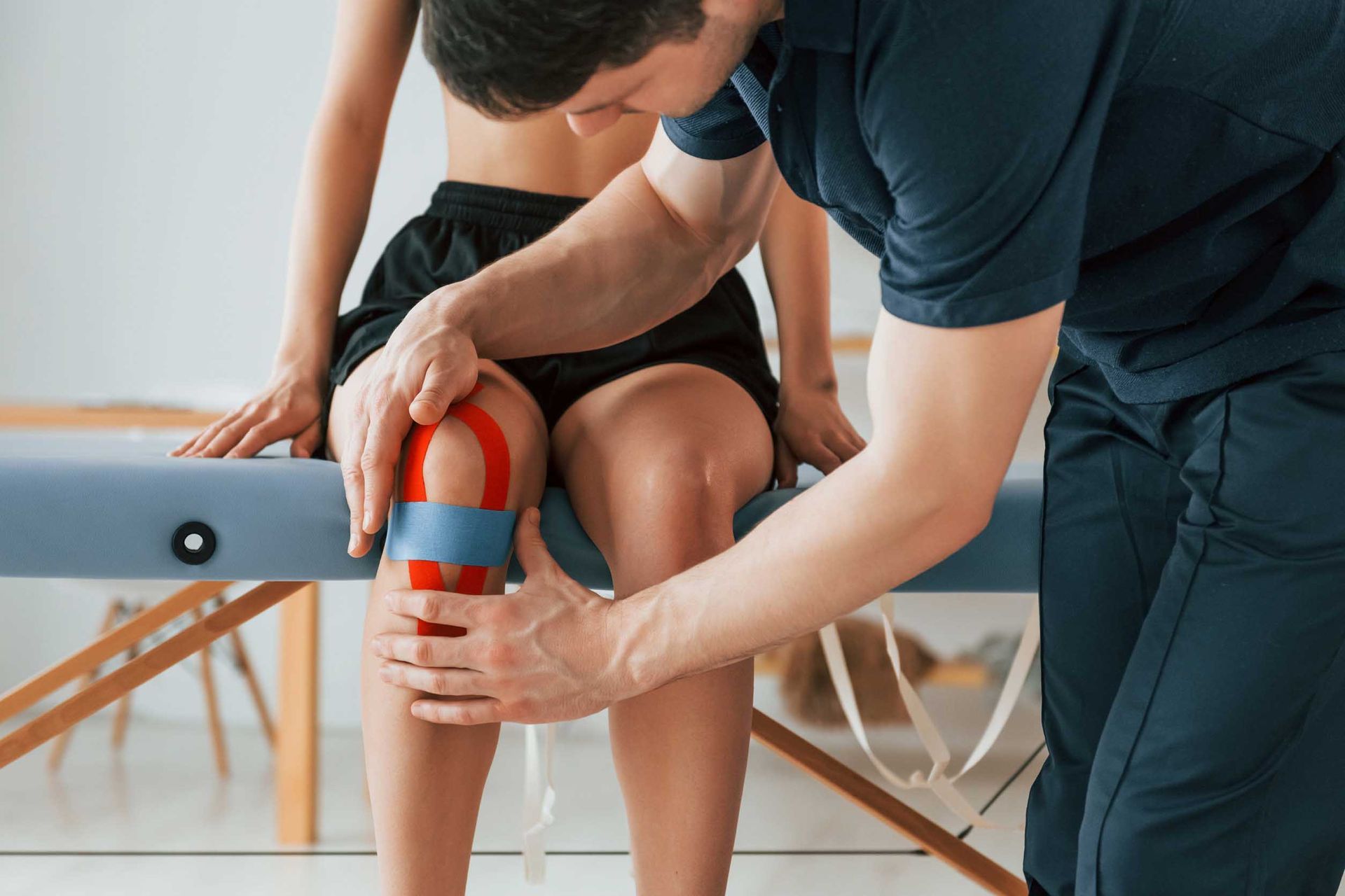 Un hombre está aplicando cinta kinesiológica en la rodilla de una mujer.