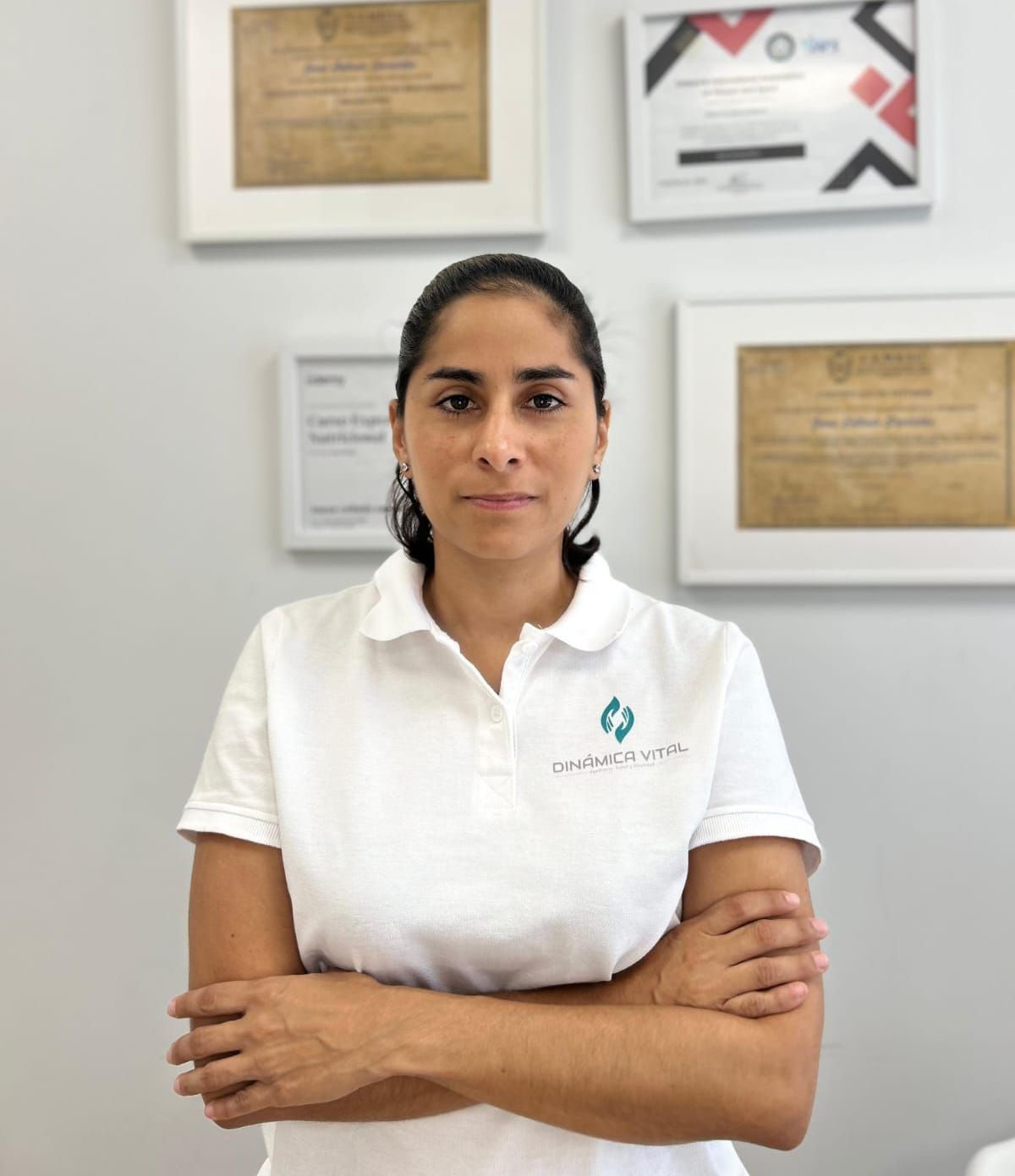 Una mujer que lleva una camisa blanca con un logotipo está de pie con los brazos cruzados.