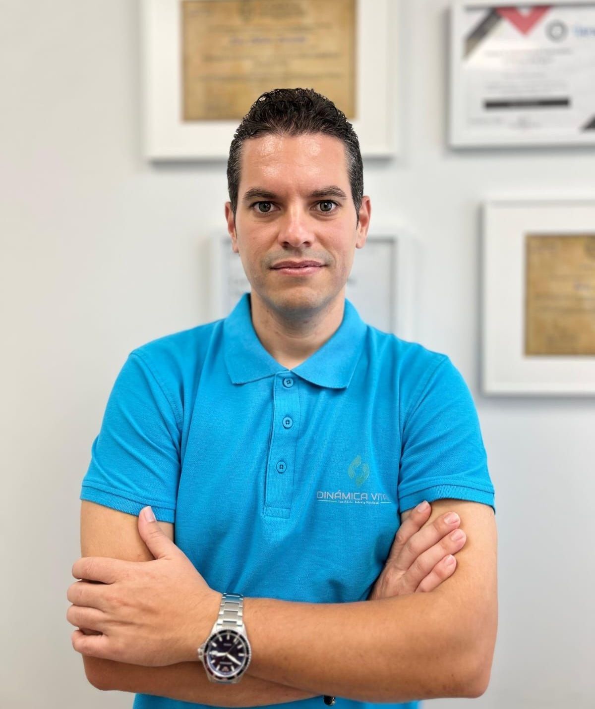 Un hombre con un polo azul está de pie con los brazos cruzados.