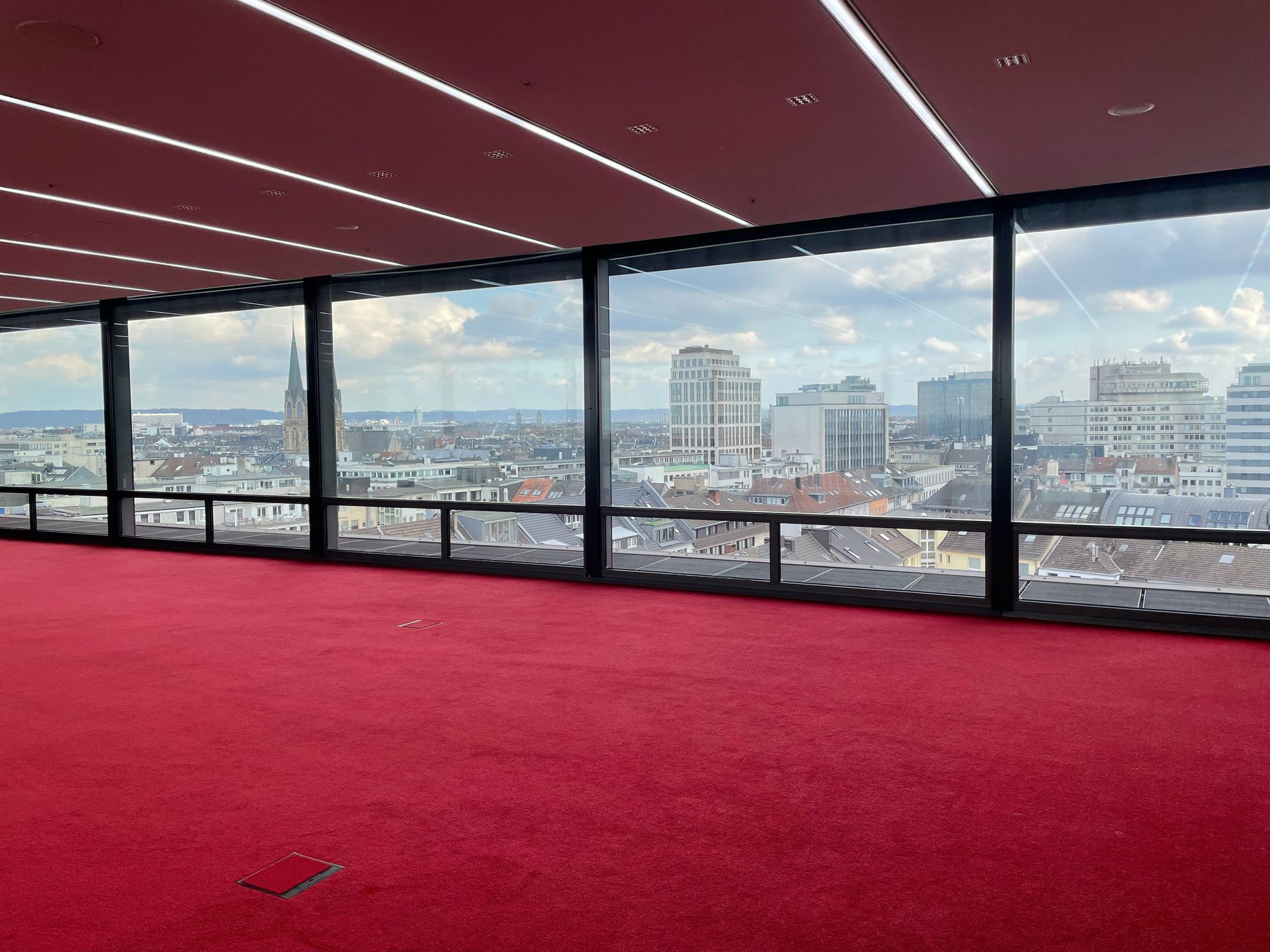Blick auf die Stadt durch große Fenster mit rotem Teppichboden.
