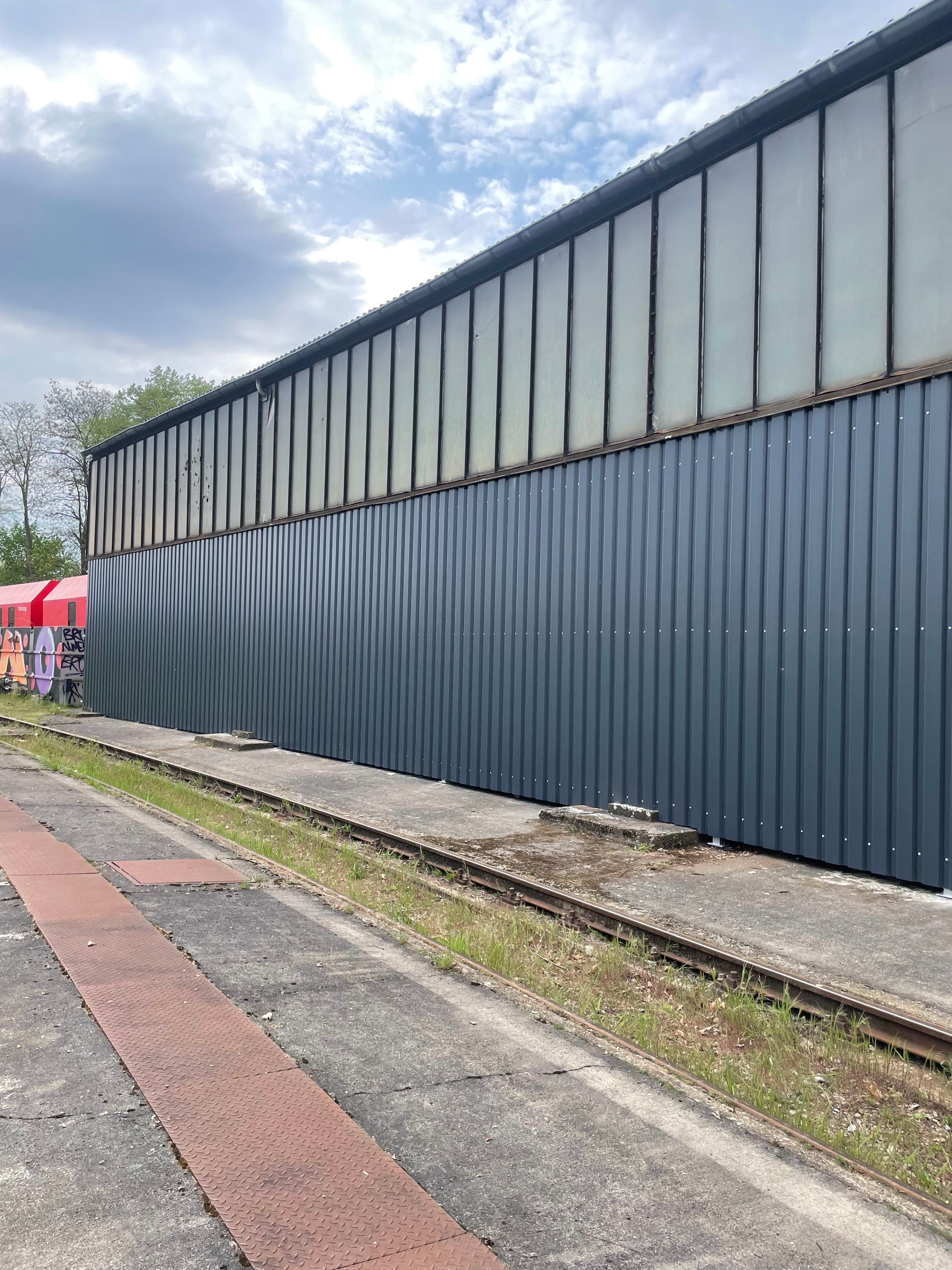 Langer, zweigeteilter Industriegebäudefassade mit oberen hellen und unteren dunkelblauen Metallpaneelen.