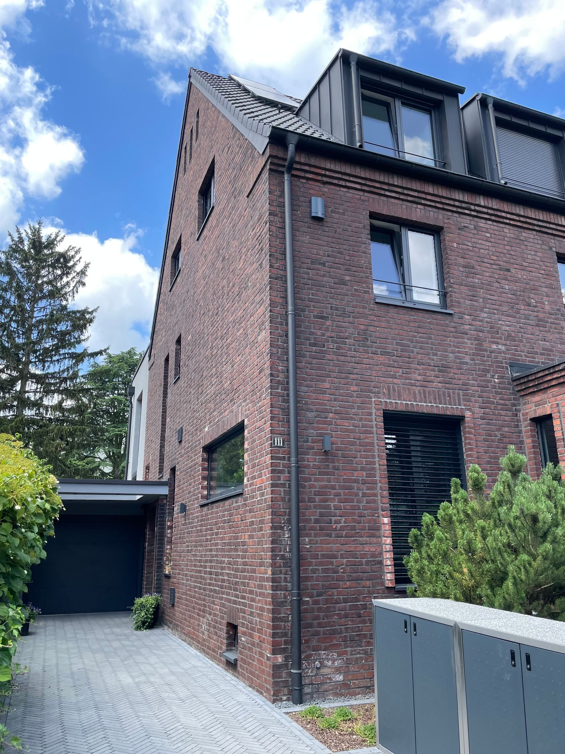 Dreistöckiges, rotes Backsteinhaus mit dunklem Dach, mehreren Fenstern und angrenzender Garage.