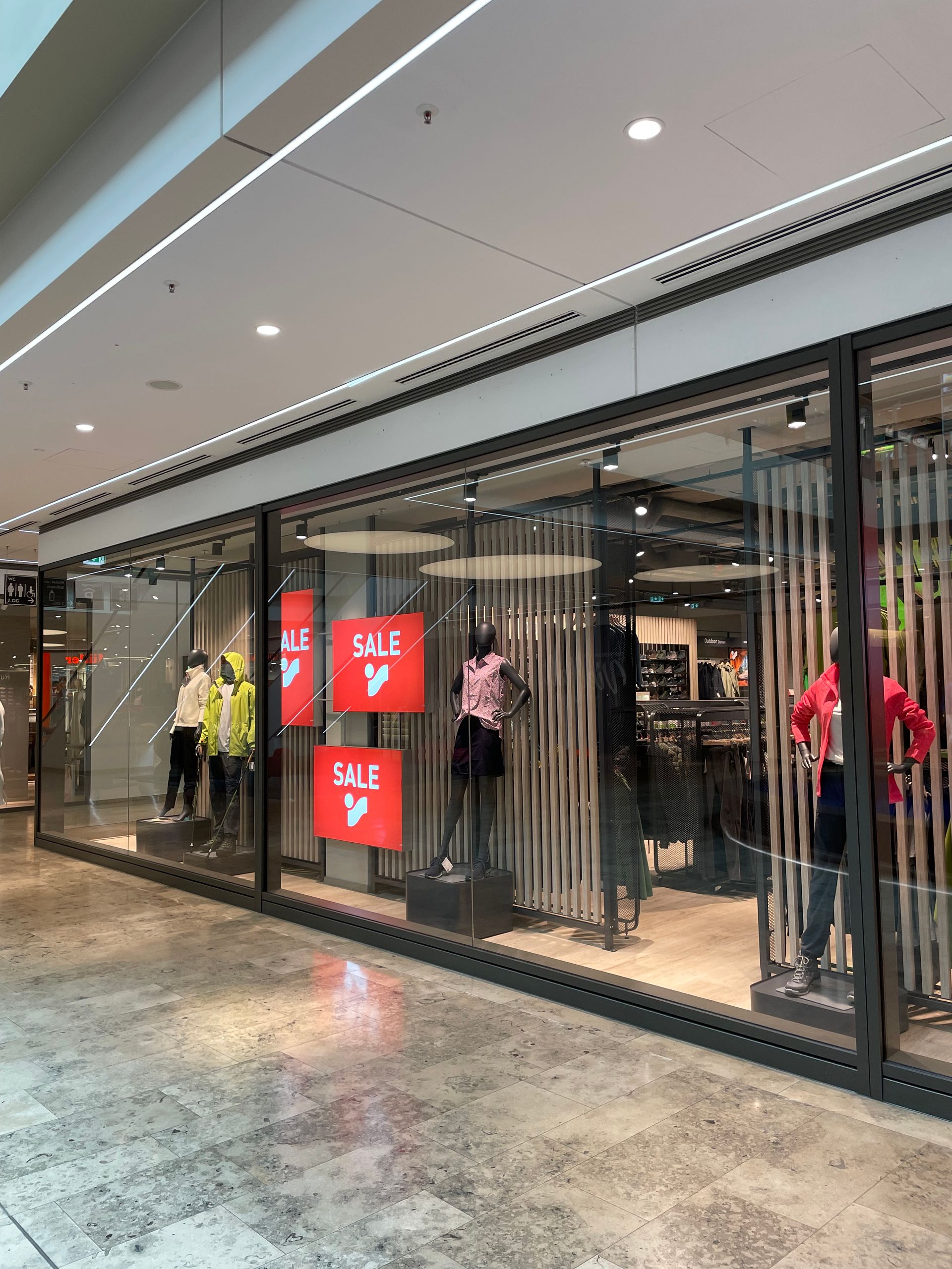 Schaufenster mit mehreren Schaufensterpuppen in bunter Kleidung und roten SALE-Schildern in einem Einkaufszentrum.