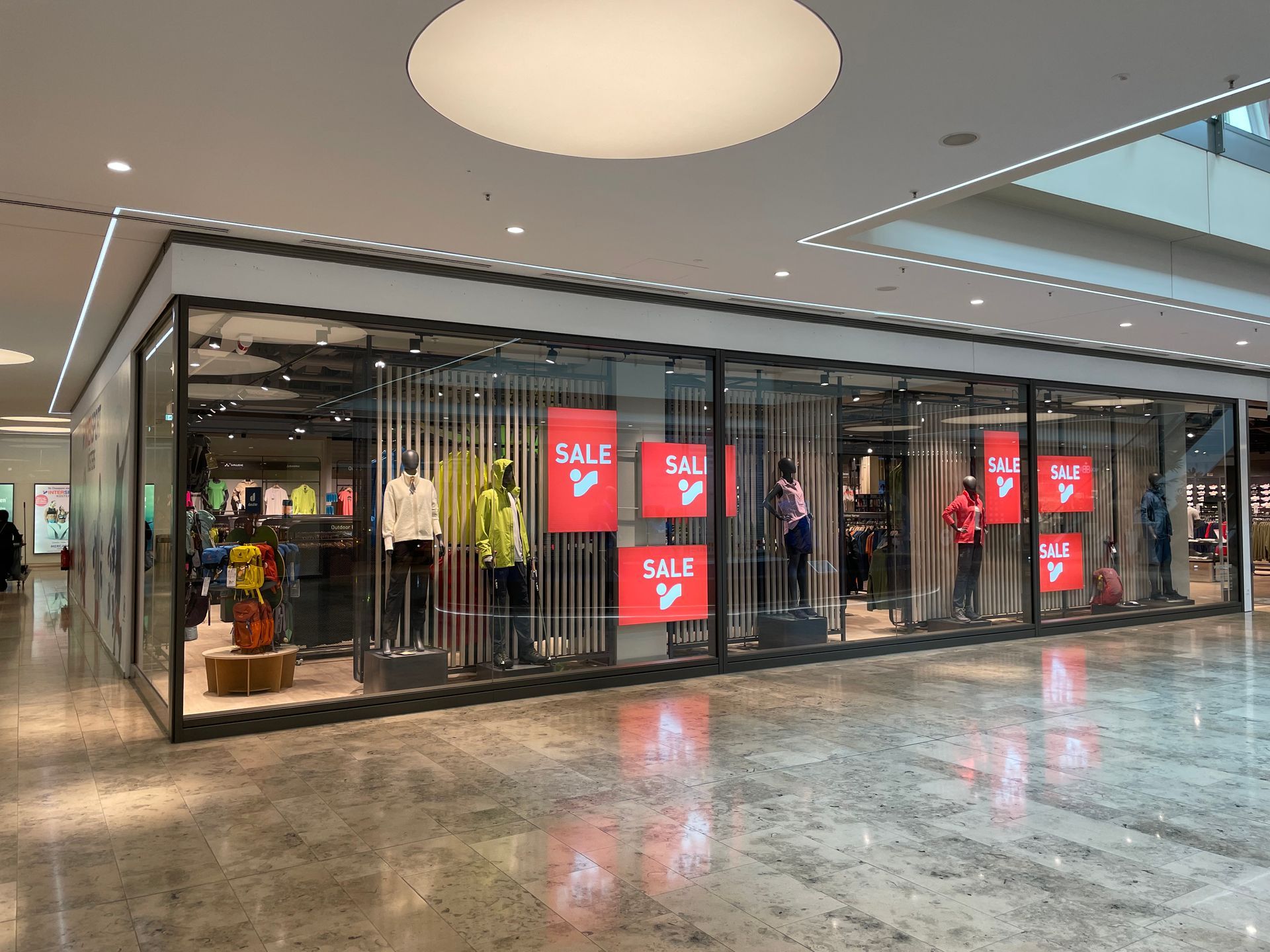 Geschäftsfront mit großen Glasfenstern, mehreren Schaufensterpuppen in bunter Kleidung und roten SALE-Schildern.