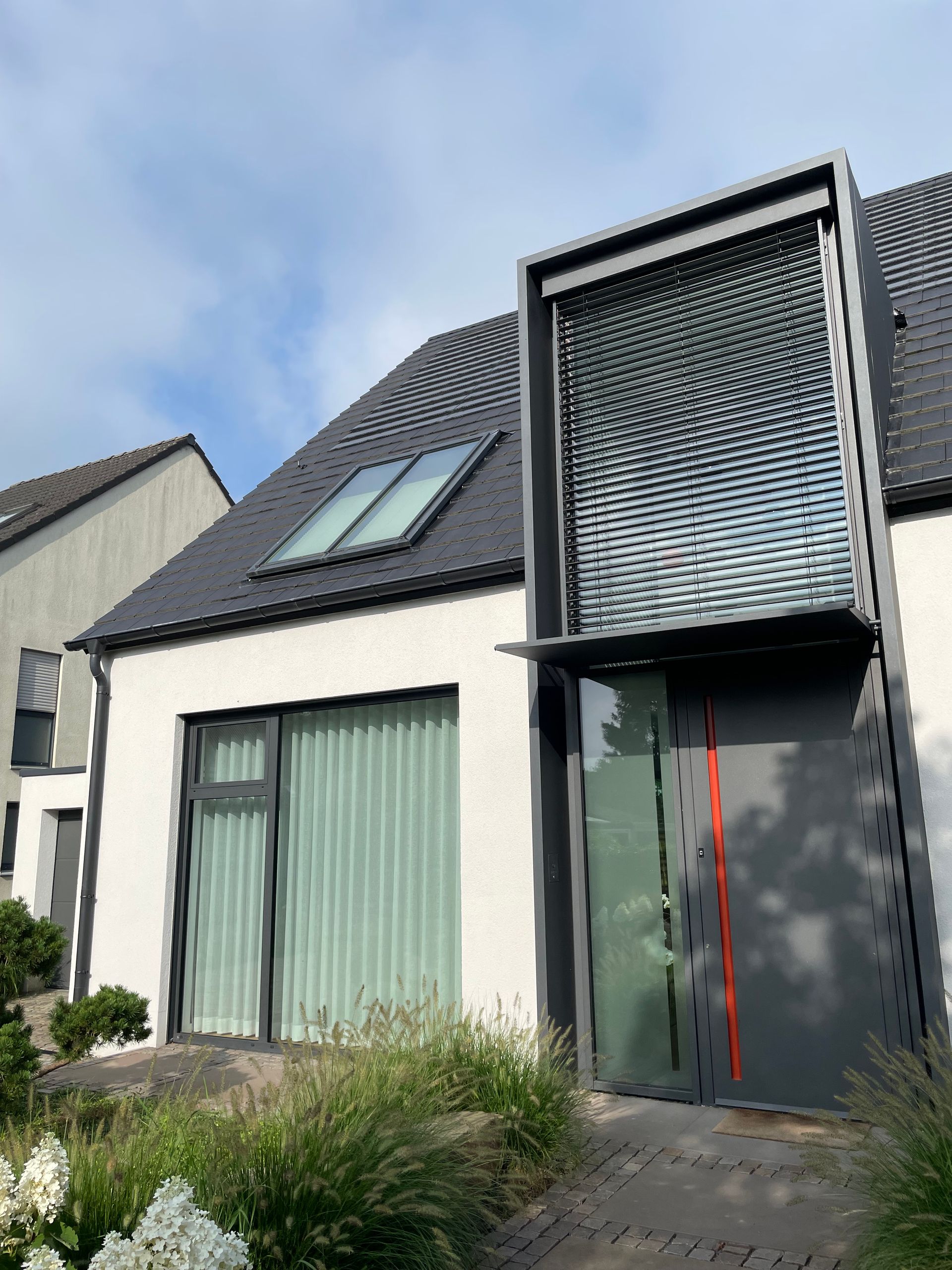 Modernes zweistöckiges Haus mit weißer Fassade, großem Fenster mit Vorhängen, dunklem Eingang .