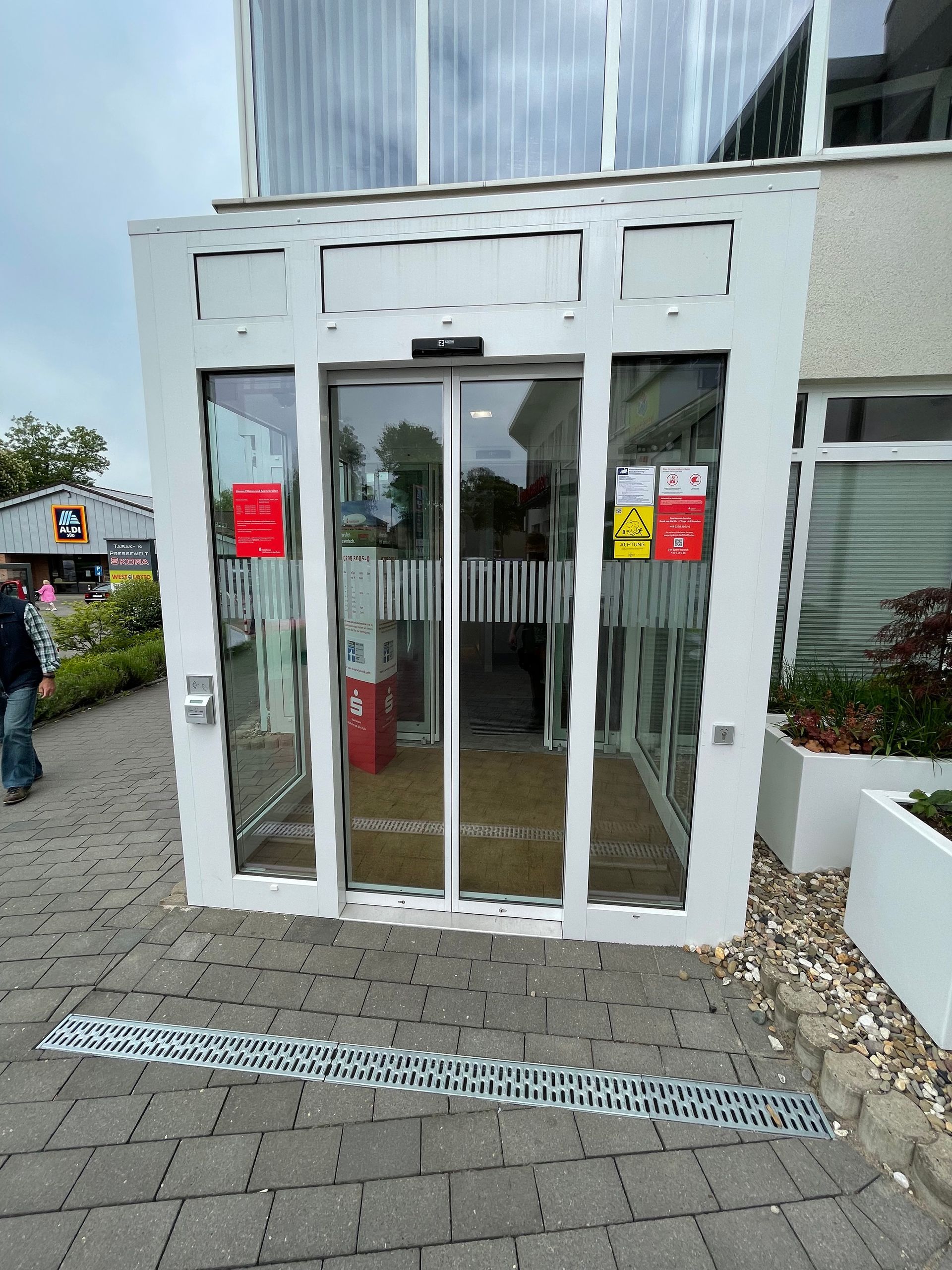 Automatische Glastür mit zwei Schiebetüren und Sicherheitsaufklebern an einem modernen Gebäude.