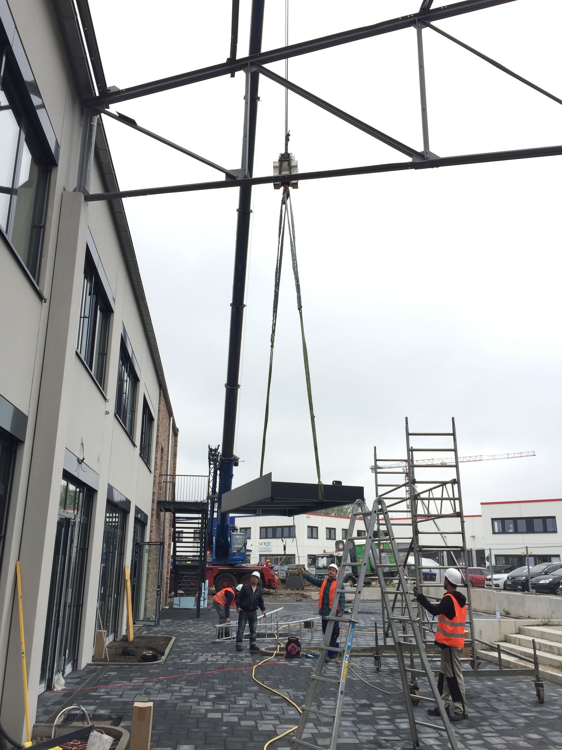 Mehrere Bauarbeiter mit Warnwesten und Helmen arbeiten auf einer Baustelle neben einem mehrstöckigen Gebäude.