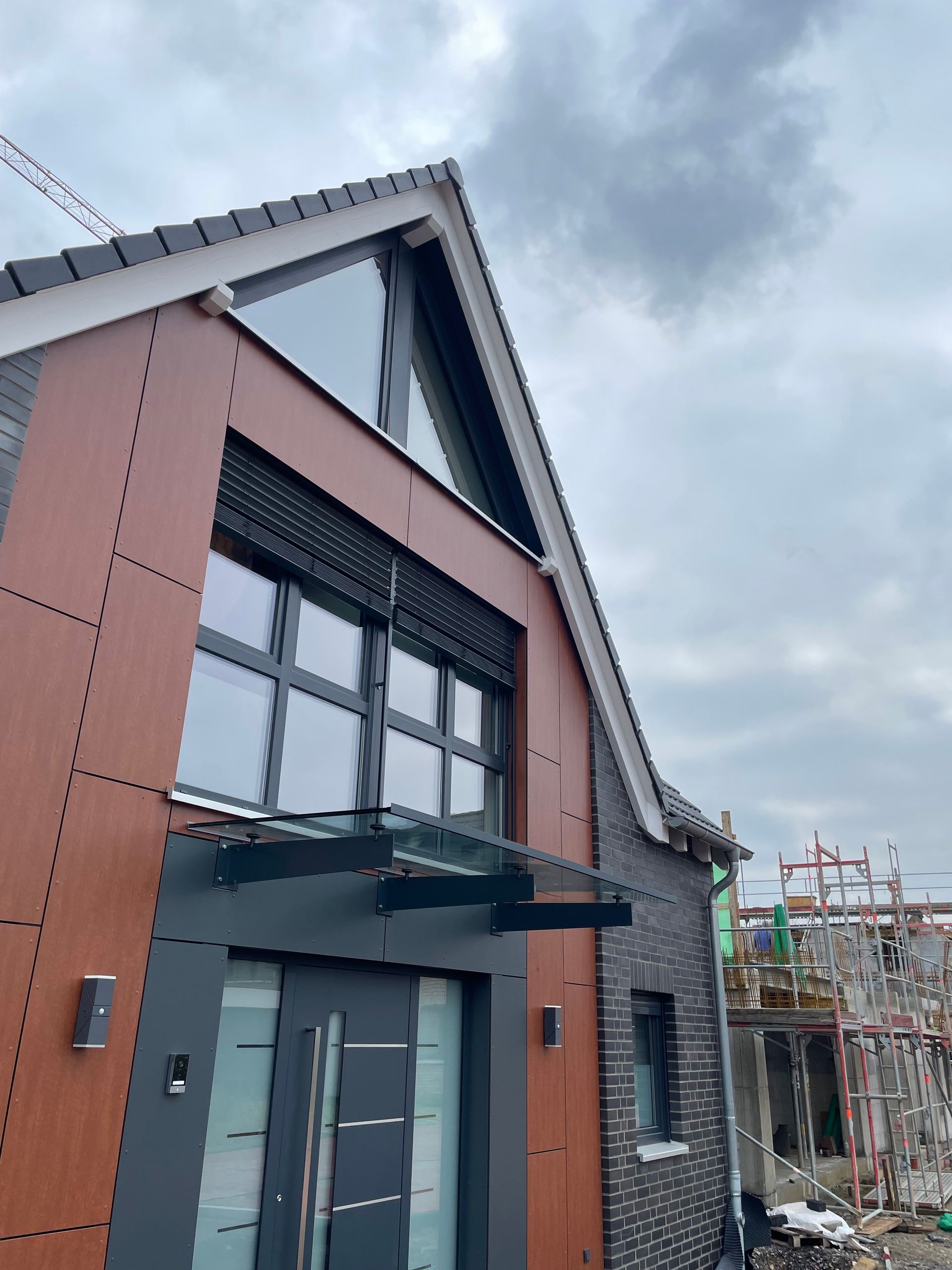 Fassade eines modernen Hauses mit braunen und schwarzen Fassadenplatten, großem Fenster.