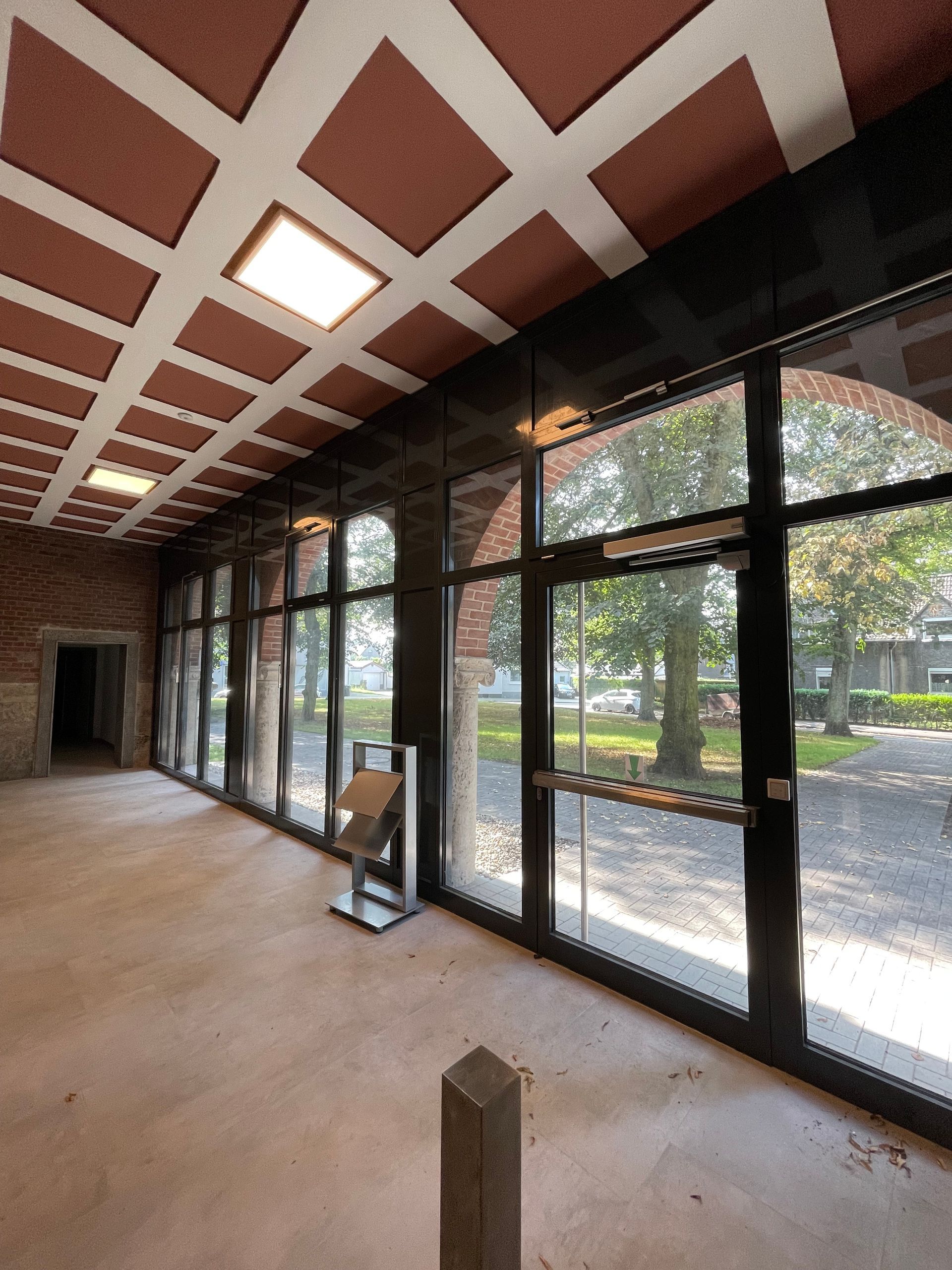 Große Glasfront mit schwarzen Metallrahmen und Bogenfenstern, Blick auf Bäume und Gehweg.