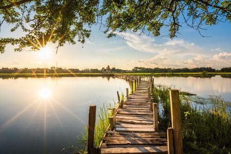 eine Holzbrücke führt über einen See bei Sonnenuntergang .