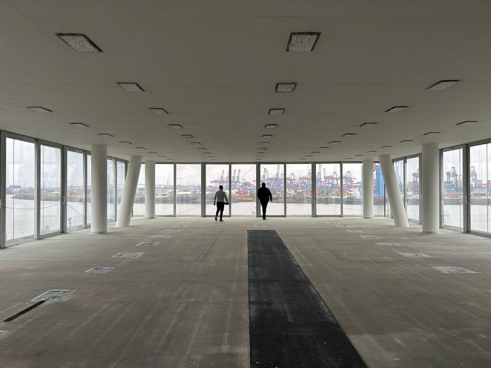 Zwei Menschen gehen durch einen leeren Raum mit vielen Fenstern, Tool Time NRW GmbH