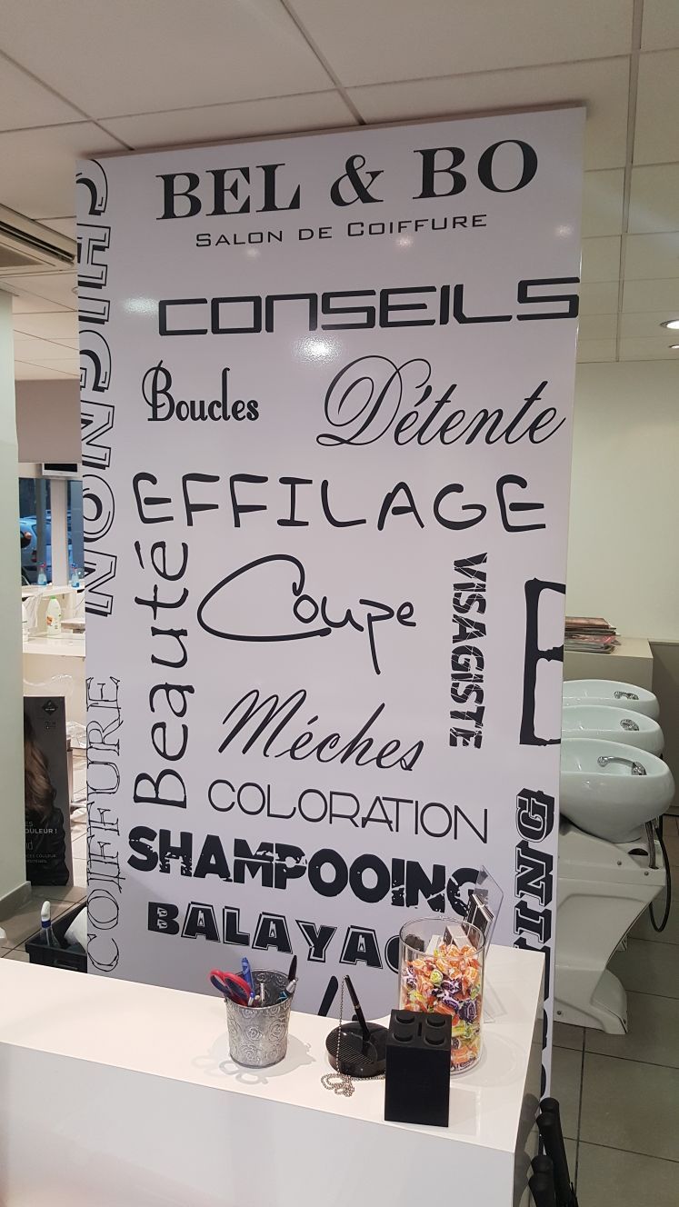 Enseigne pour un salon de coiffure, avec les noms des services proposés en caractères noirs sur fond blanc.
