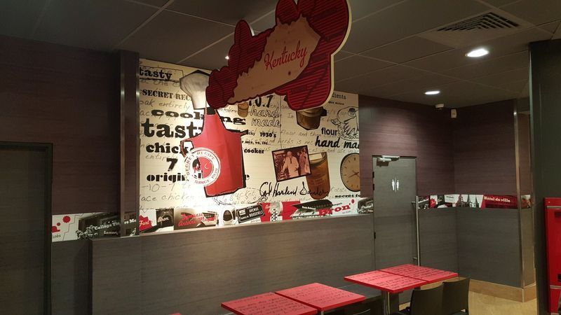 Intérieur d'un restaurant de restauration rapide. Décor rouge et noir, avec des tables, des œuvres d'art murales et une mascotte à l'envers.