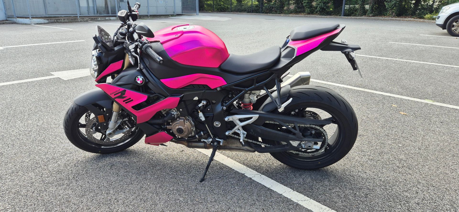 Une moto sport BMW, d'un magenta et d'un noir éclatants, garée sur l'asphalte d'un parking.