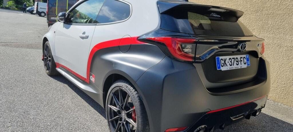 Une Toyota GR Yaris blanche, noire et rouge garée à l'extérieur sur une surface asphaltée, vue de trois quarts arrière.