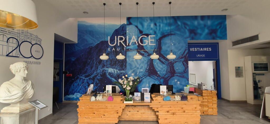 Un comptoir d'accueil avec un mur bleu à l'effigie de la marque, un comptoir en bois et une sculpture de buste blanc dans un espace intérieur moderne.