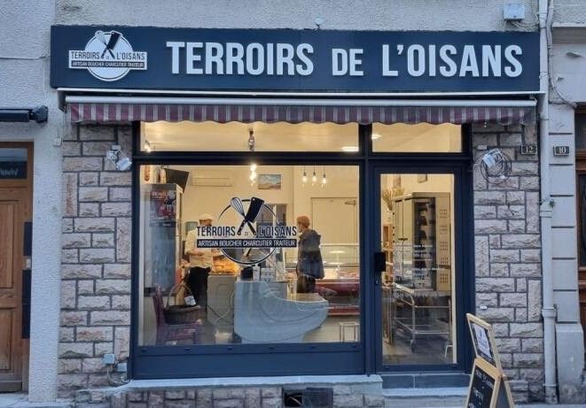 Une devanture de magasin nommée Terroirs de l'Oisans avec une façade en pierre, des vitrines et une enseigne bleu foncé au-dessus.
