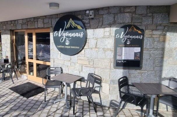 Terrasse extérieure du restaurant Le Vyonnais avec un mur en pierre, des tables et des chaises devant une porte en bois.
