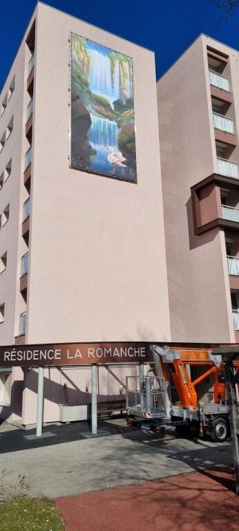 Un immeuble d'appartements roses nommé Résidence La Romanche arbore une grande fresque verticale représentant une cascade sur son mur latéral.