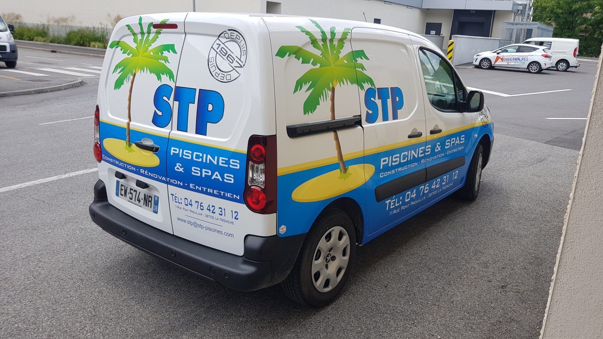 Camionnette blanc et bleu ornée d'un logo en forme de palmier, garée sur le trottoir.
