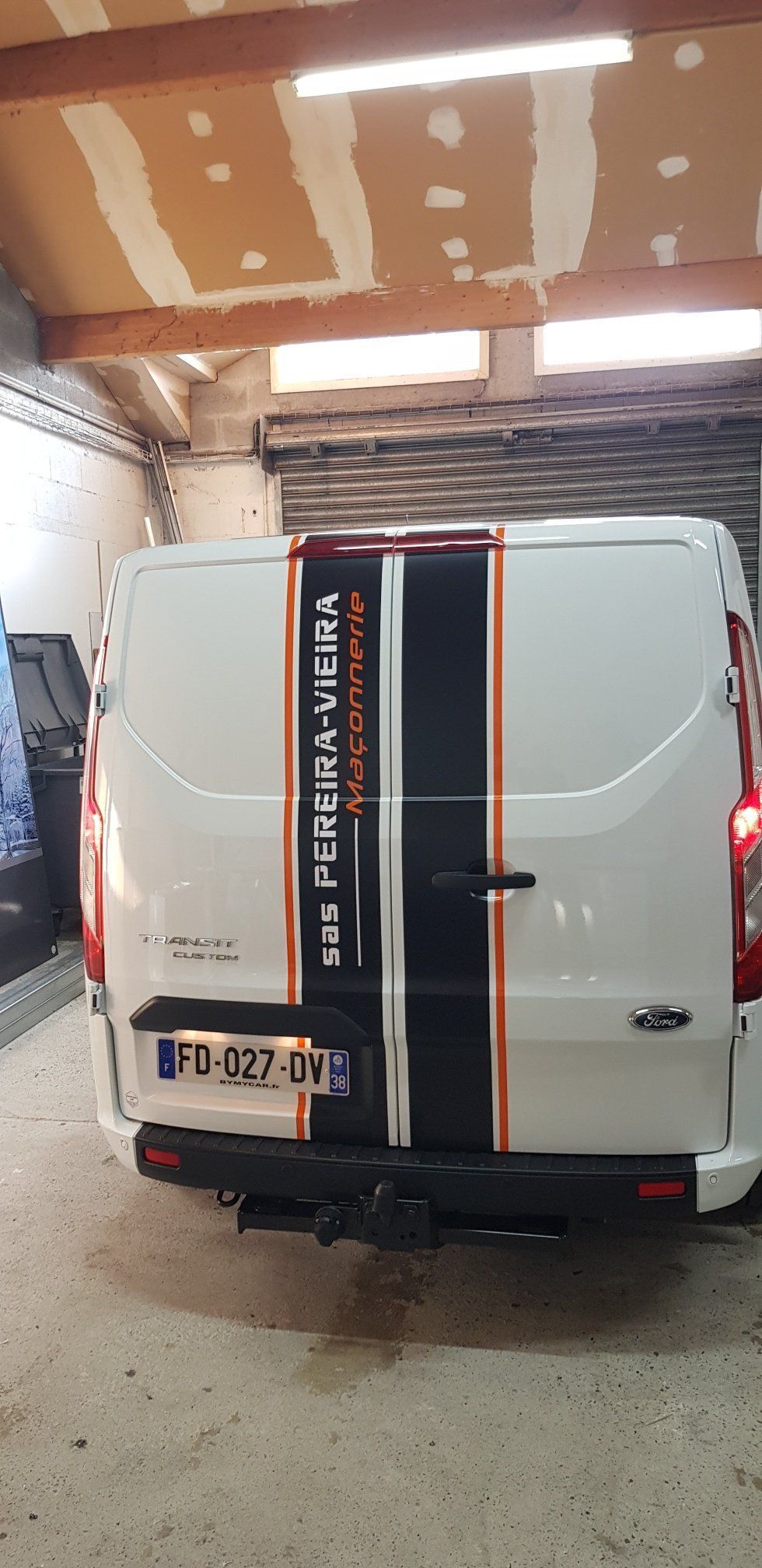 Fourgonnette blanche avec une bande noir et orange. La fourgonnette se trouve dans un garage.