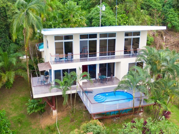 Modern two-story tropical house with a balcony and small blue pool surrounded by lush greenery