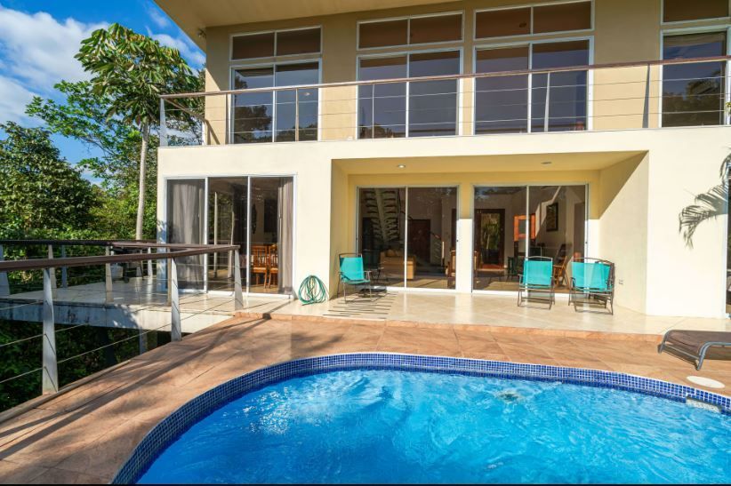 Modern two-story house with a swimming pool and patio seating in bright sunlight