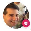 Smiling person in a circular profile photo with a pink shield badge overlay