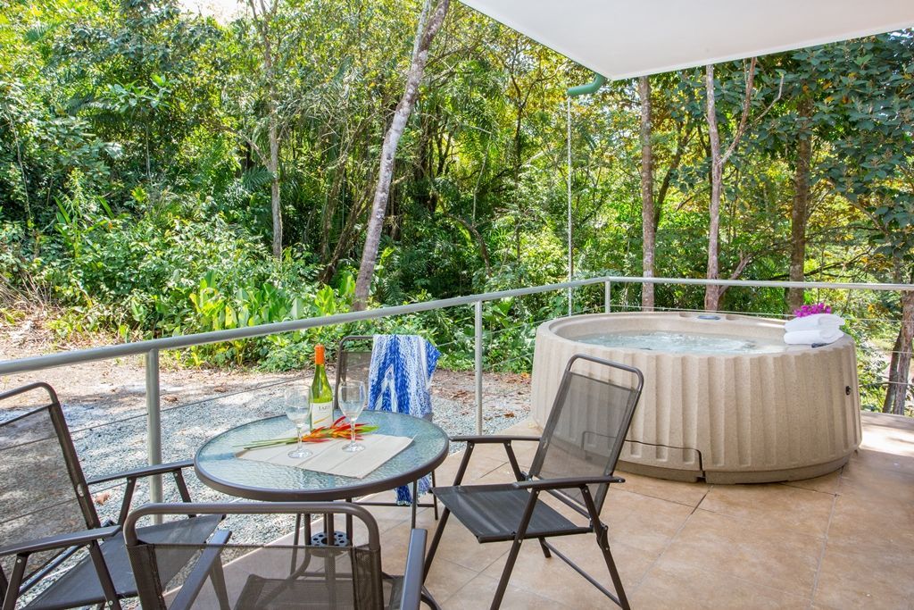 Outdoor patio with table and chairs overlooking lush greenery, with a covered hot tub nearby