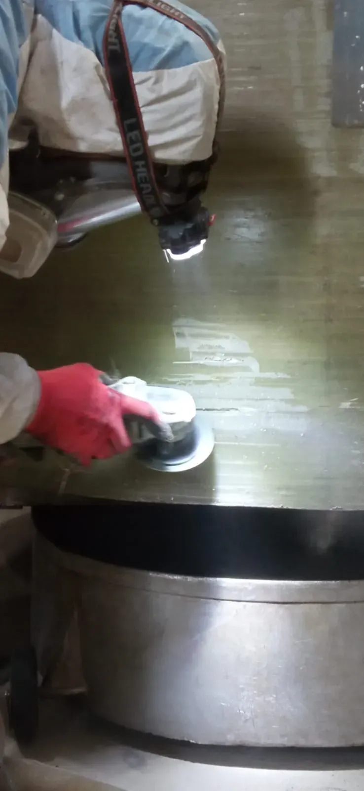 Persona con traje de protección aplica sellador a una superficie azul en un tejado, con edificios al fondo.