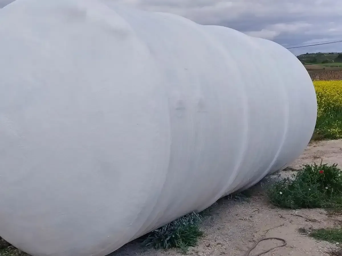 Tanque cilíndrico blanco tendido de lado en el exterior, posiblemente utilizado para almacenamiento.