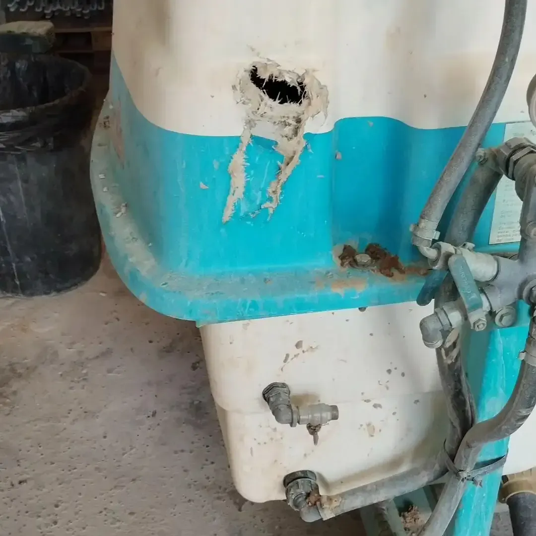 Contenedor de plástico blanco y verde azulado dañado con un agujero grande.