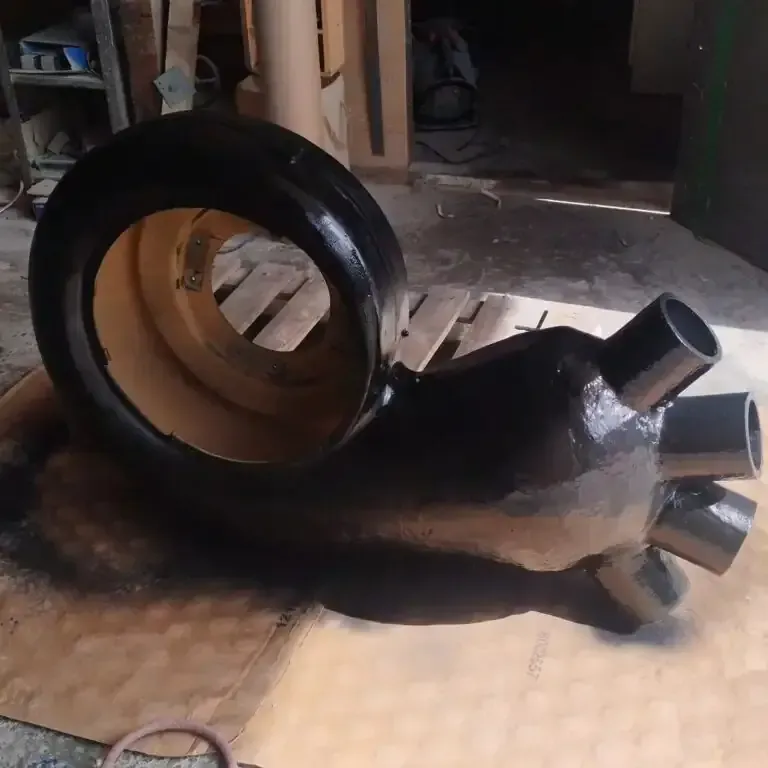 Escultura de caracol pintada de negro, realizada a partir de un neumático y otros materiales sobre una superficie marrón.