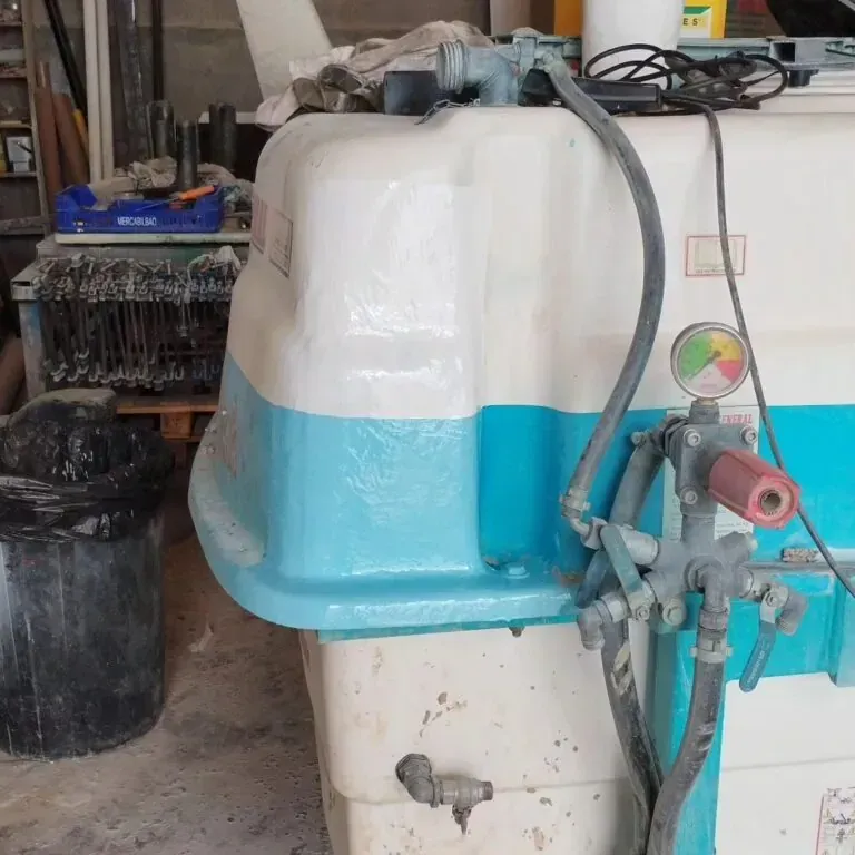 Gran máquina industrial de color blanco y verde azulado con mangueras y válvulas en un entorno de taller.